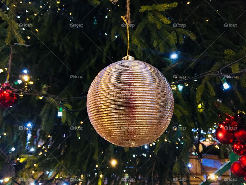 Giant golden Christmas globe hanging on the Christmas tree outside with lights in the background 