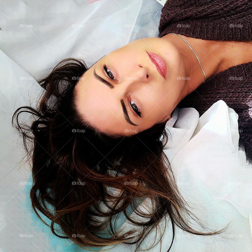 Selfie portrait of a woman who lies on a white background. Highlighted hair combed back