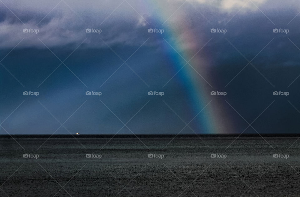 A beautiful rainbow was created by rays of sunshine breaking through the clouds. The rays of light also lit a small boat alone in the strait making for home harbour before those dark storm clouds came any closer.  