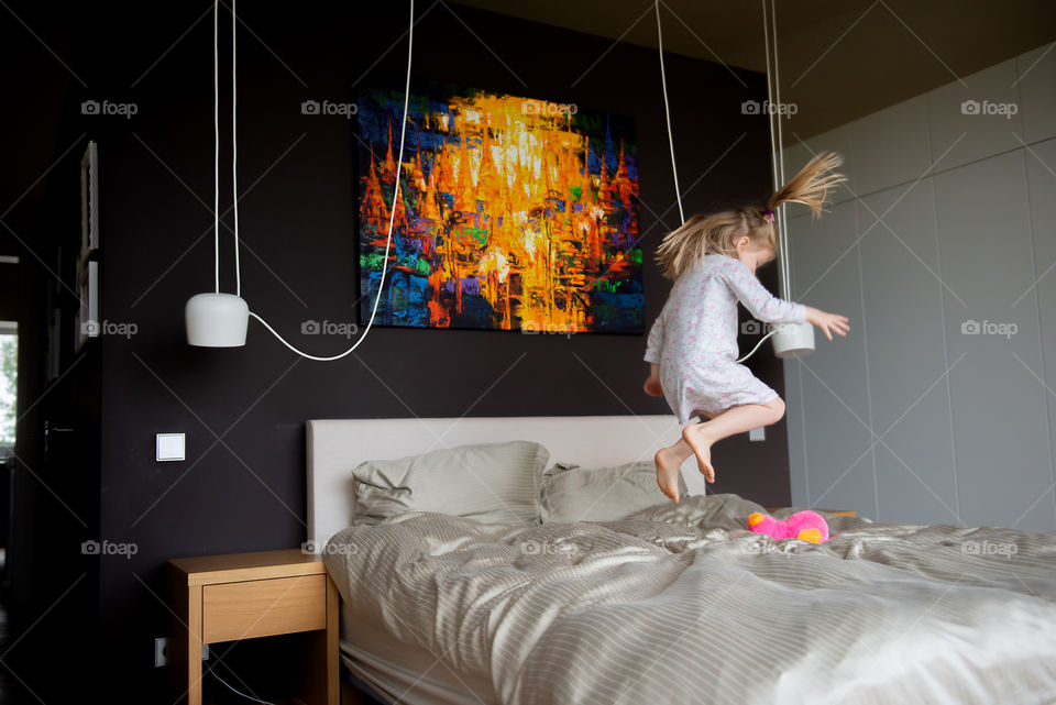 Happy child girl having fun jumps and plays bed