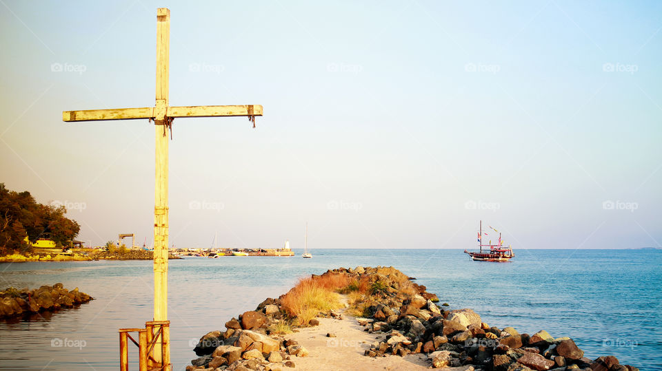 Catholic wooden cross on the seashore, landscape with a sailboat in the bay