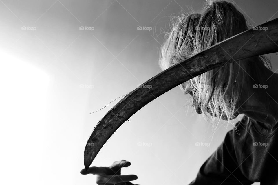 Black and white photo of a woman checking the sharpness of a scythe with her finger