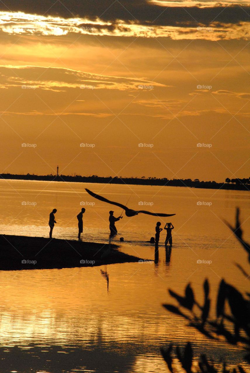 golden orange sunset creates silhouettes of family enjoying the last few moments of the day at the shoreline