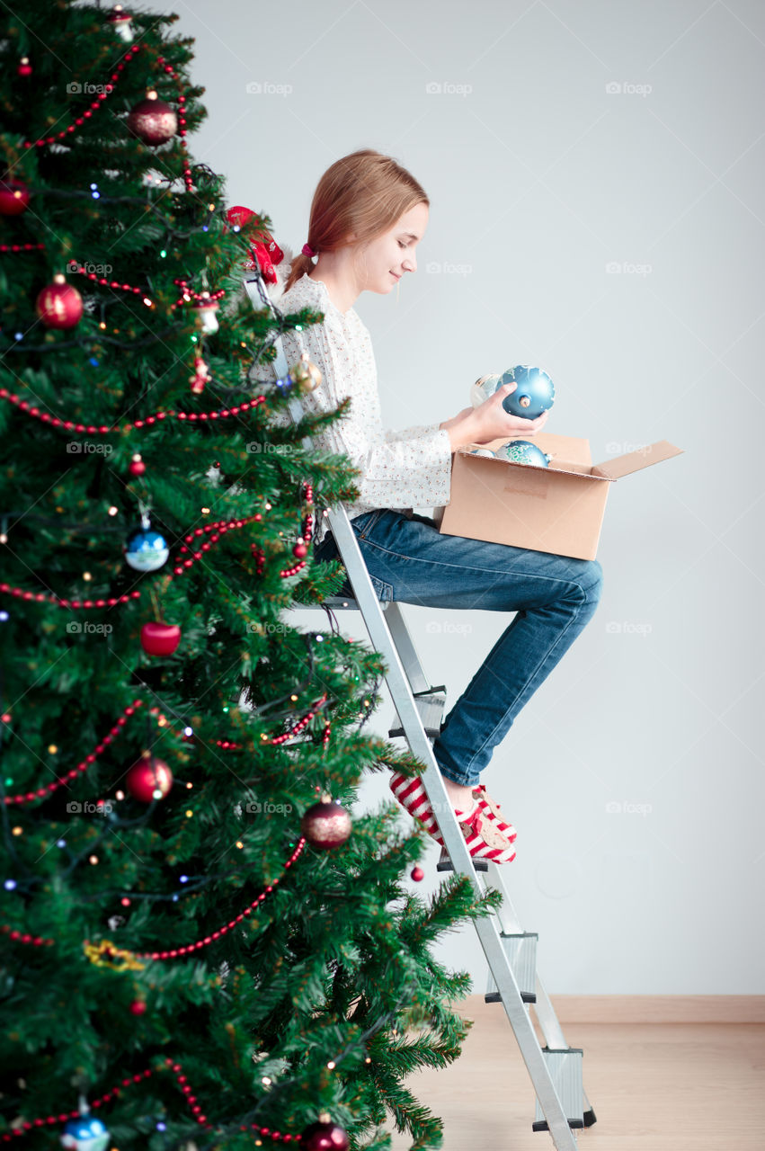 Teenage girl sitting on ladder near christmas tree