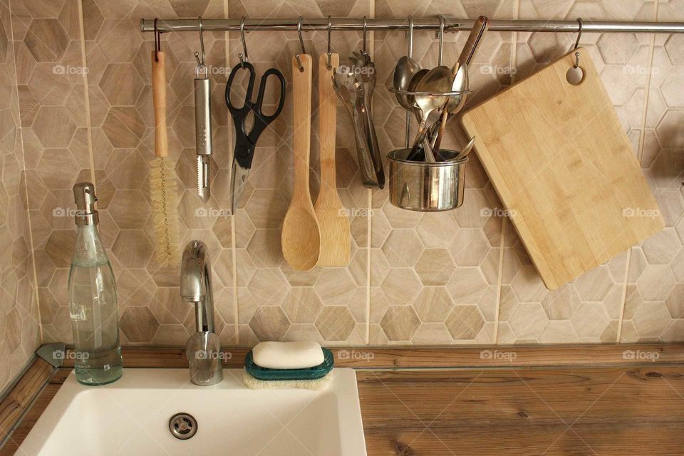 White sink with wooden and steel kitchen utensils in the kitchen in eco scandy style