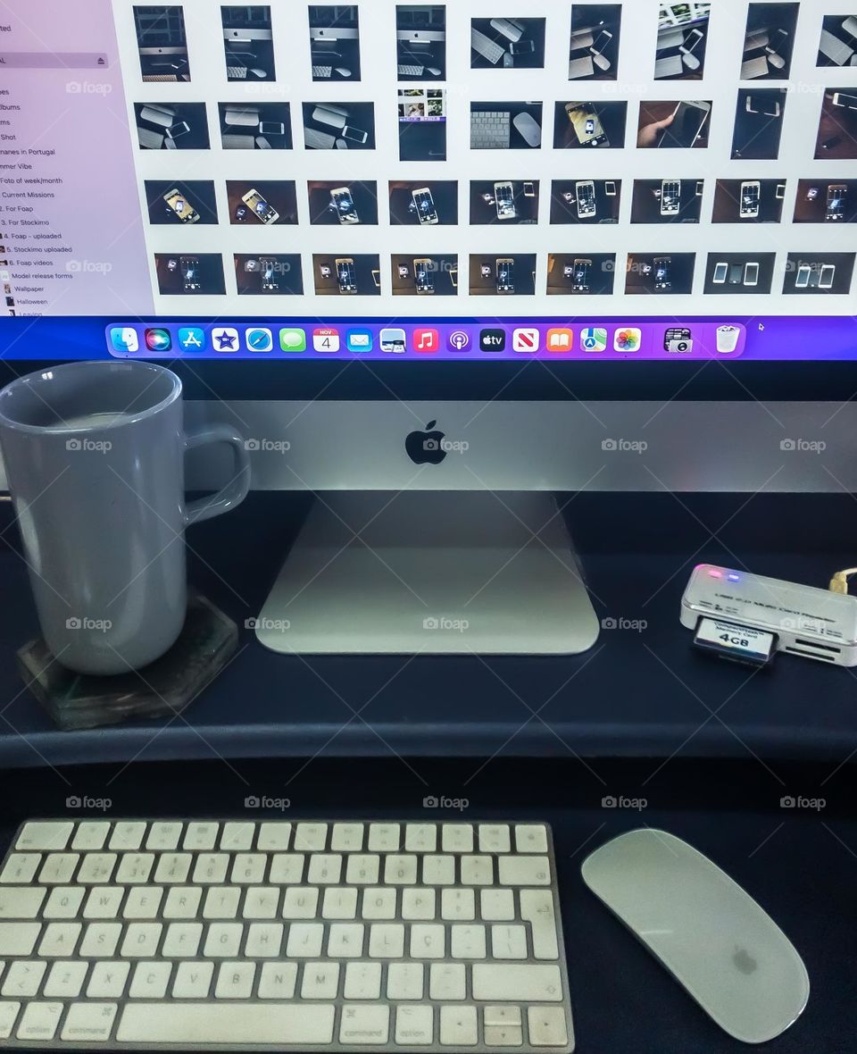 View of an iMac on a purple desk with iPhotos open. There is a cup of coffee to one side and a memory card plugged in, also with keyboard and mouse.