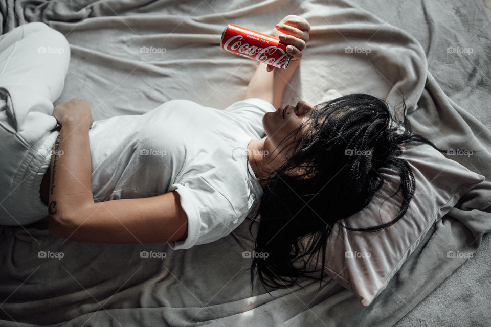 the girl lies on the bed and holds a Coca Cola