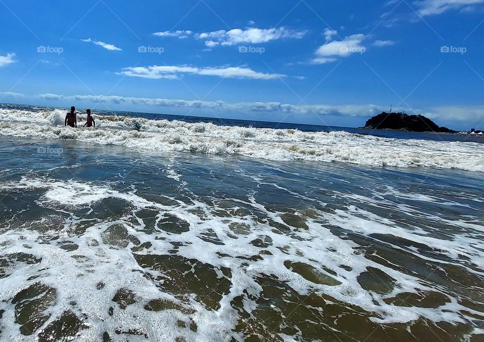O mar, o céu azul, o avô e o neto, duas crianças felizes pulando as ondas.