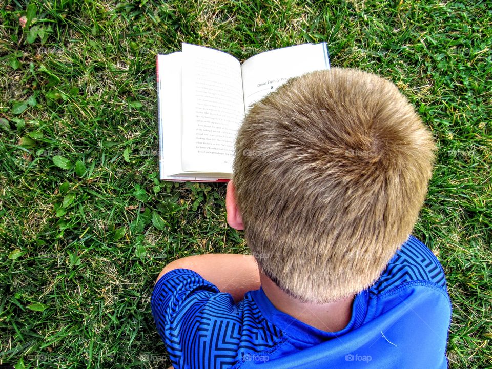 blond boy reading a book in the grass