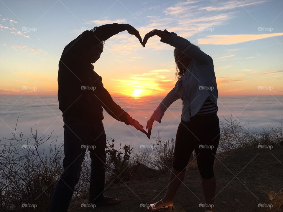 Couple forming heart shape frame of sunset.