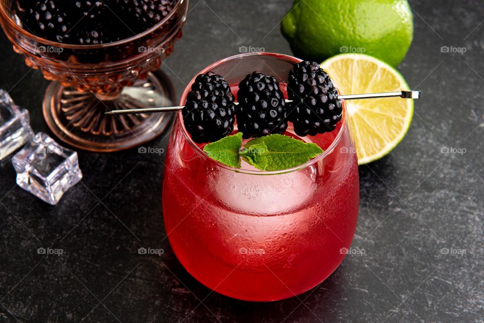 Closeup image of a colorful blackberry cocktail in a glass over ice with limes 