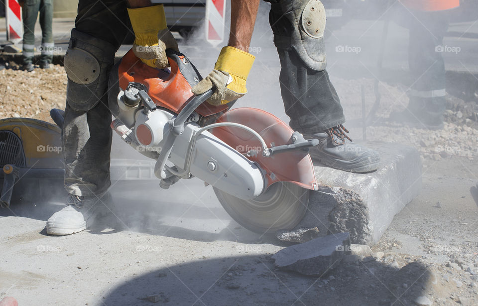 Builder worker with cut-off machine power tool breaking concrete at road construction site