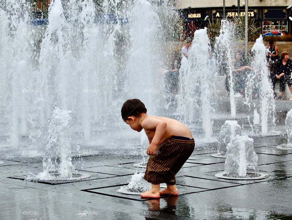 Young child playing in a fountain in the centre of Manchester, England, on a hot summer day. 