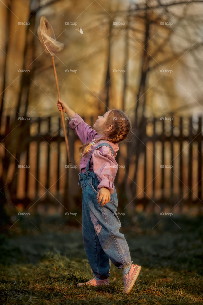 Little girl with butterfly net outdoor at sunset