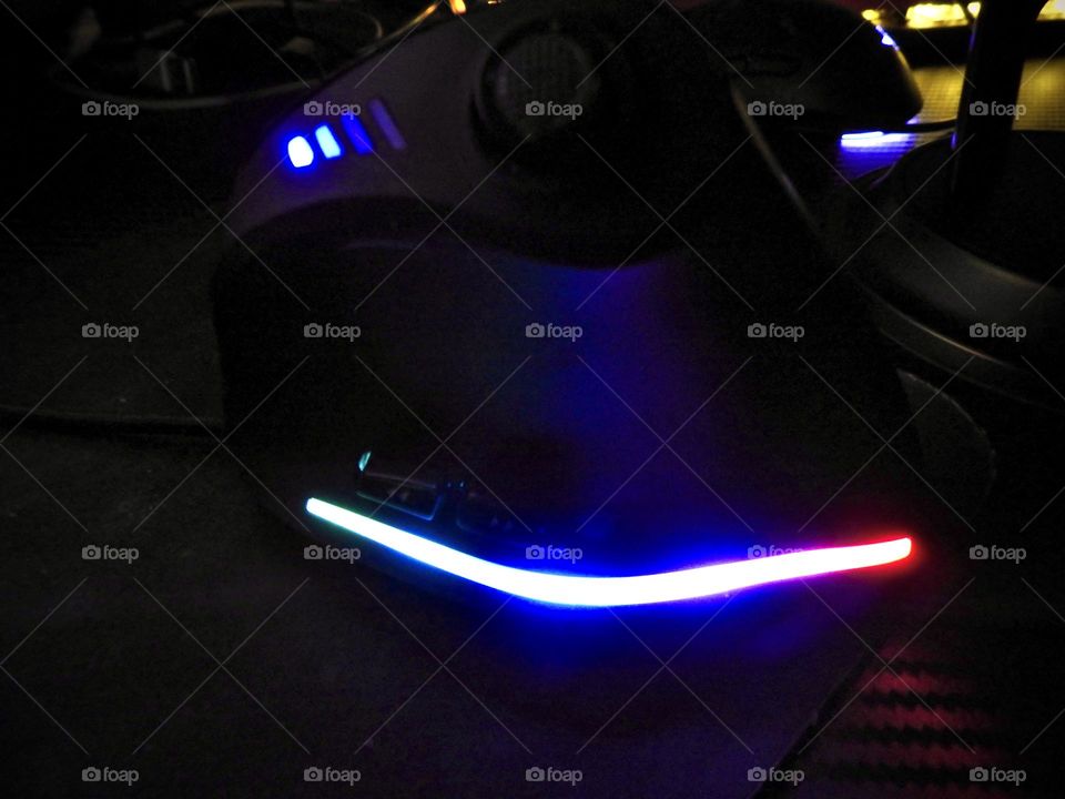 Gaming set focusing on the mouse showing accessories in a dark room enhancing the beautiful effect with the illuminating of different color lighting through them on a gaming desk.