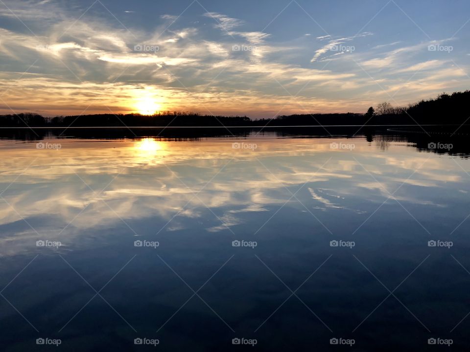 Stunning sunset over glass surface of lake in late winter. 