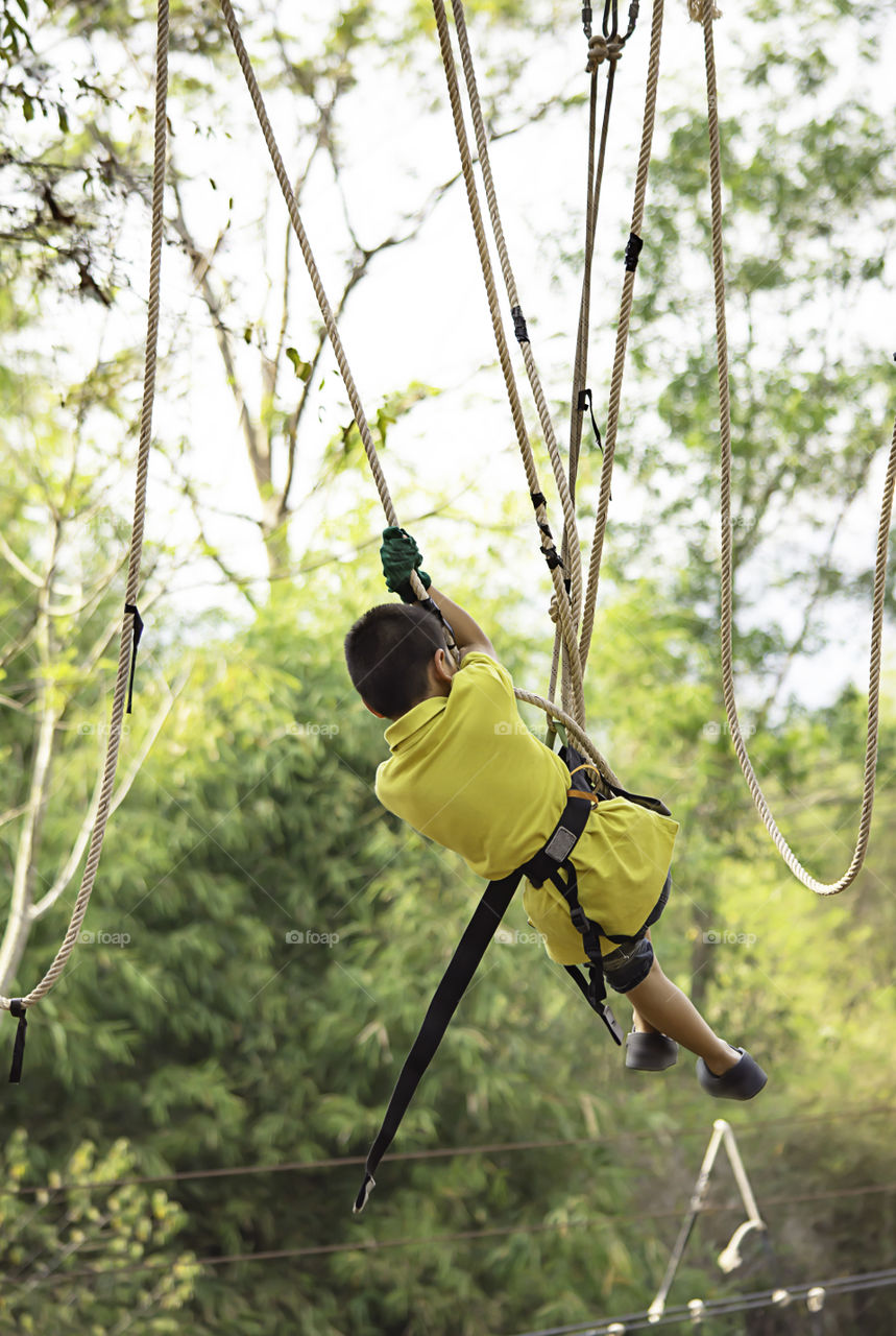 Asean boy nodes the rope and smiling happily in camp adventure Background blurry tree.