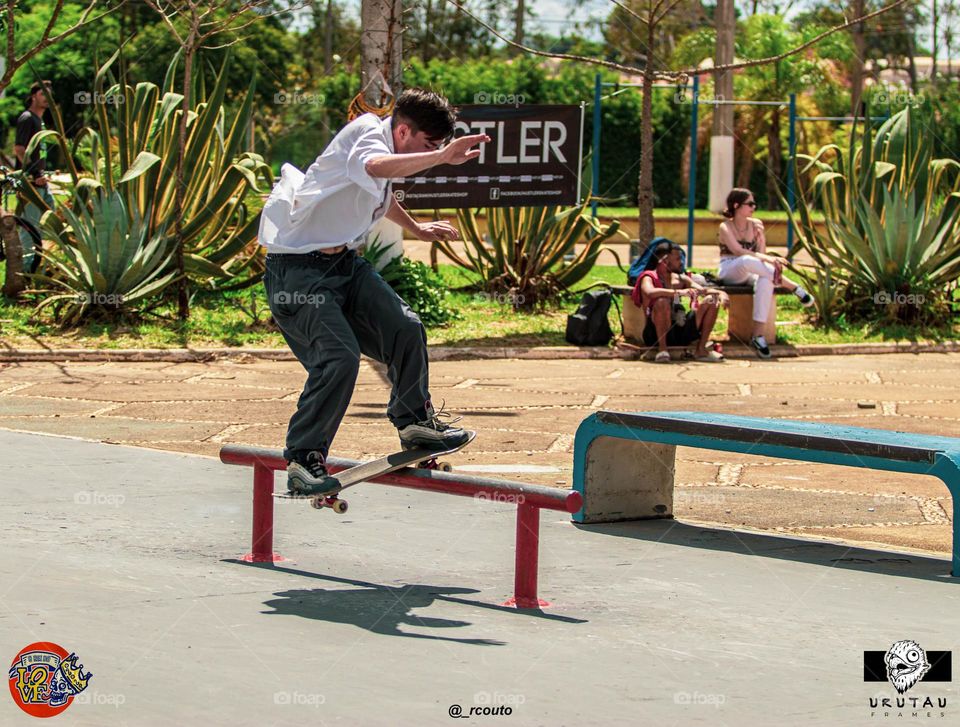 Skatista realizando manobra sobre obstáculo em pista de skate em dia ensolarado e bonito.