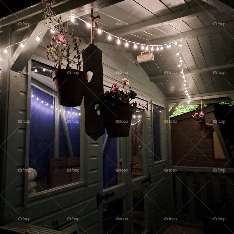 summerhouse at night lit with fairylights hanging under roof.
