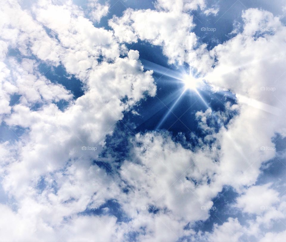 See The Light. Blue sky and white clouds with sun rays streaming through.
