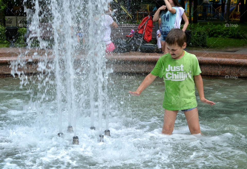 child boy in water fountain urban nature summer time