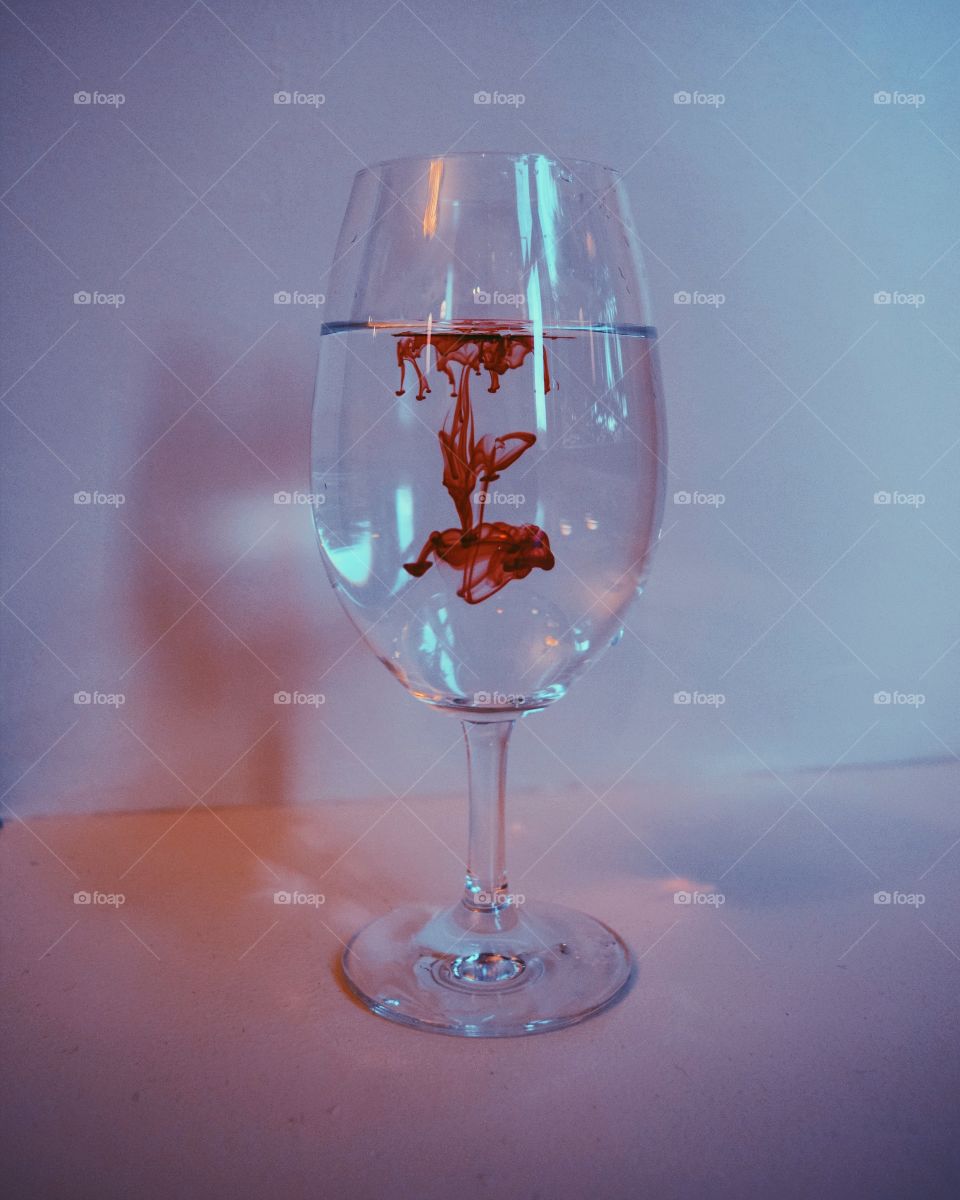 A red food coloring droplet into a wineglass of water