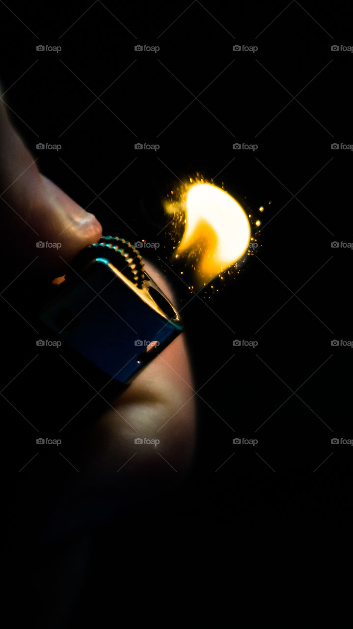 A person has lighters in his hands and he lights it through a flint wheel, the lighter ignites, sparks and fire appear, close-up on a black background.