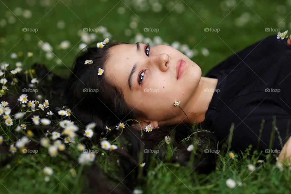 Beautiful young girl with lovely long hair lies in the grass with a little white daisies. 
Unusual shooting angle. Shooting from below. Down up. From the ground up...