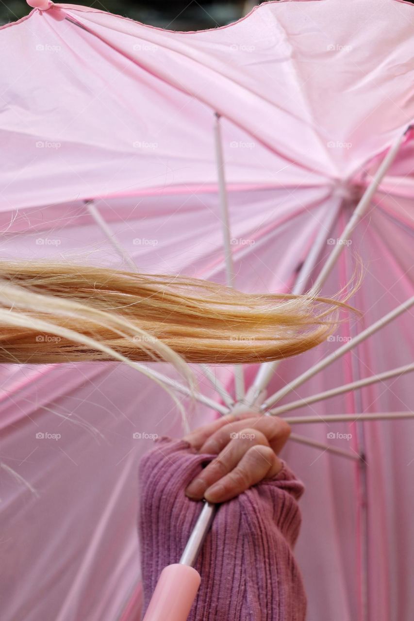 A hand holds an open pink umbrella with a blond braid in the foreground