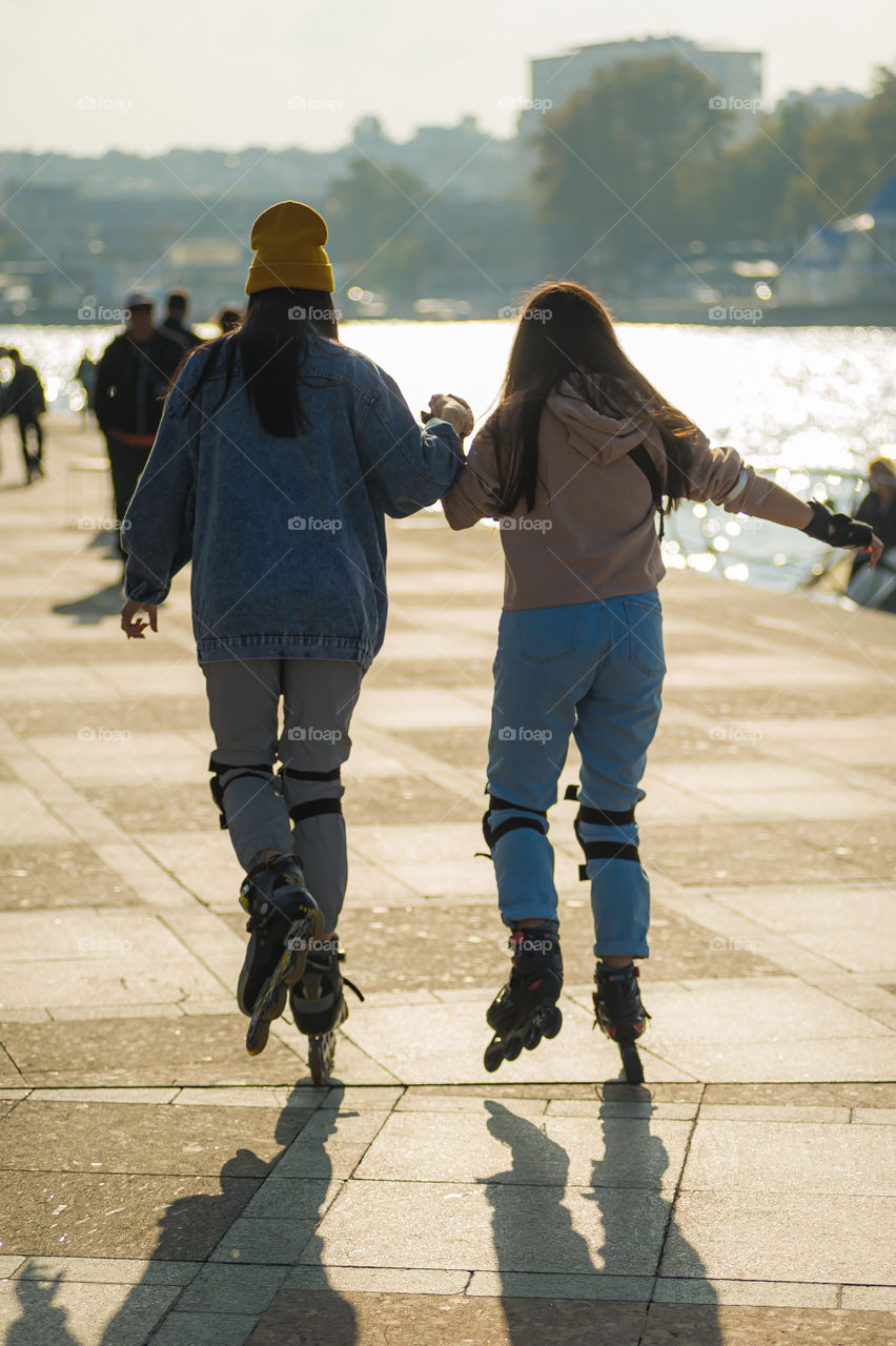 Two young girls roller-skating in the city center, on the seaside boulevard