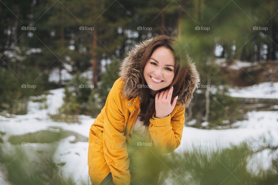 Portrait of young smiling beautiful woman in yellow jacket walking in the winter forest
