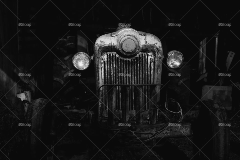 Black and white of an antique tractor dimly  illuminated by lantern light at night. 