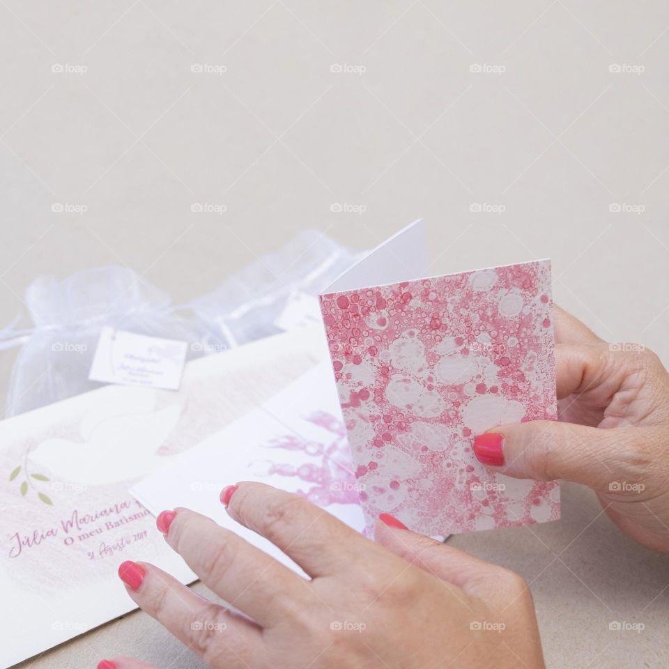 Hands showing nails with intense pink varnish and holding on to girl's christening party cards