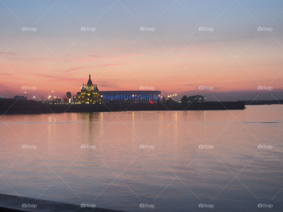 Orthodox Cathedral in the name of St. Alexander Nevsky and a football stadium in Nizhny Novgorod.  Evening lighting of buildings.  Photo on the background of the sunset.  Oka River.