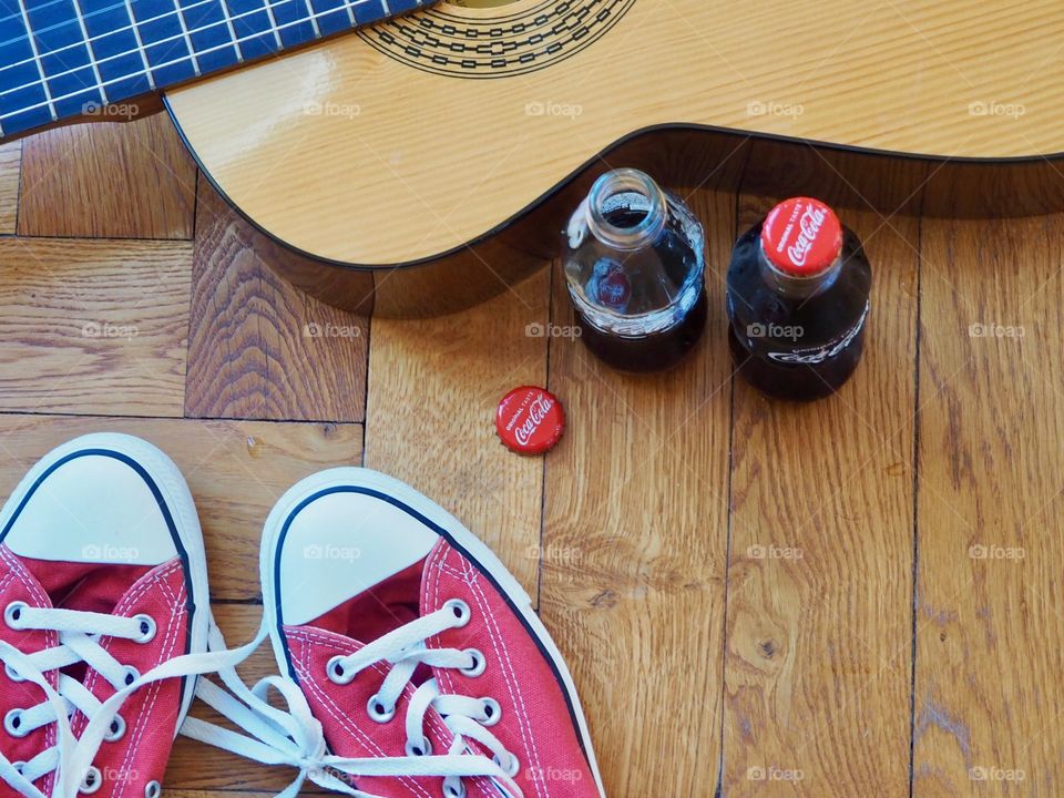 Coca Cola bottles on hardwood floor with red sneakers and guitar.