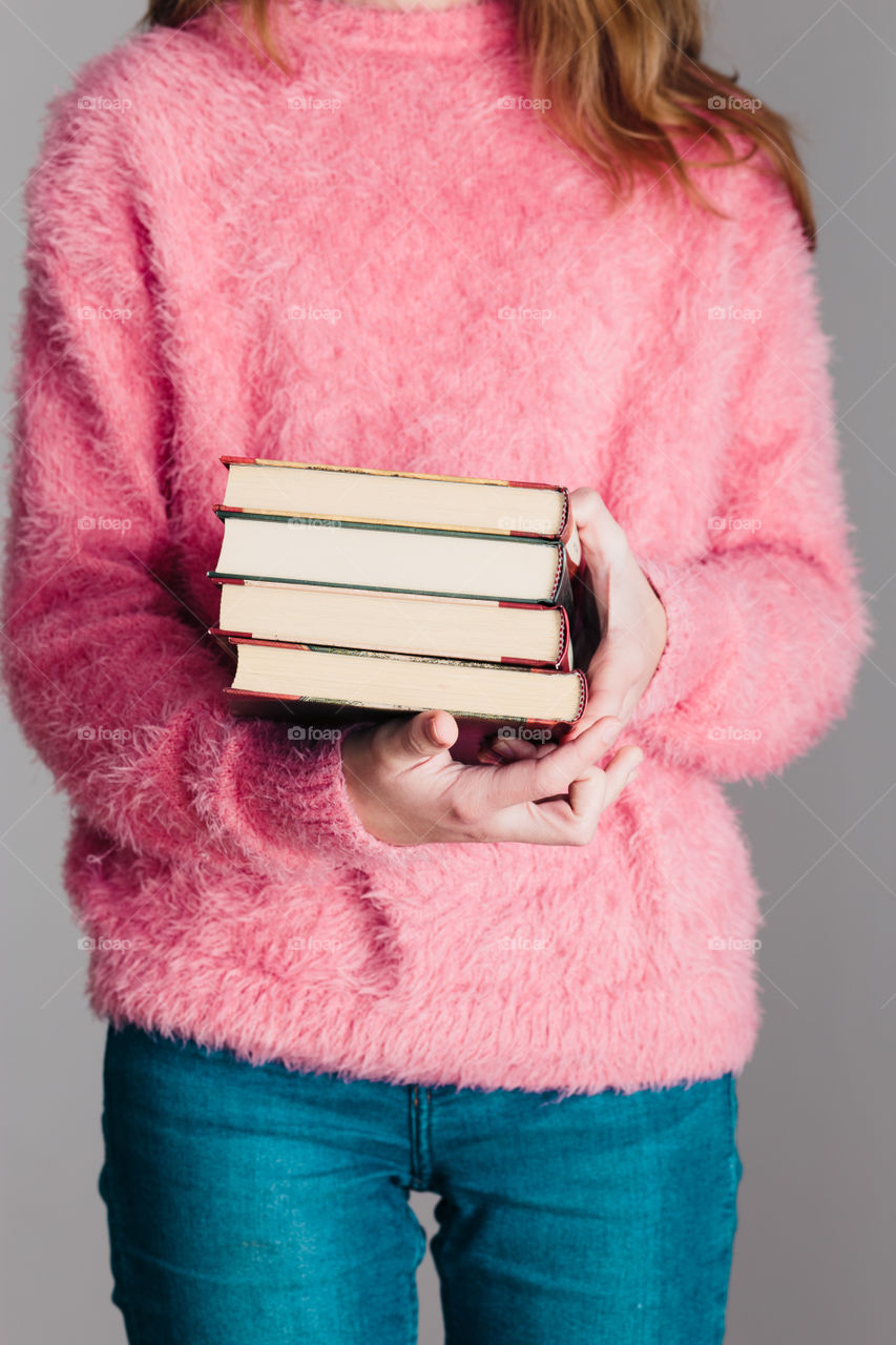 Young girl holding a few books. Teenager girl wearing pink sweater and blue jeans. Vertical photo