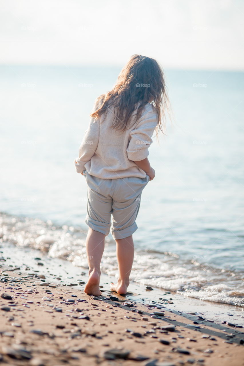 Little girl walking on the sea shore at sunny morning 