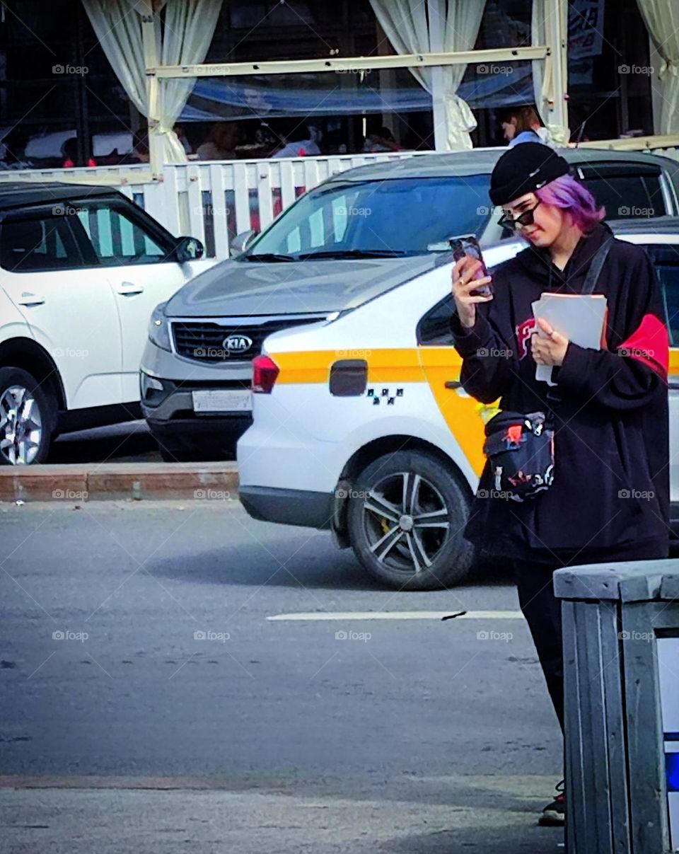 Girl with a phone and passing taxis