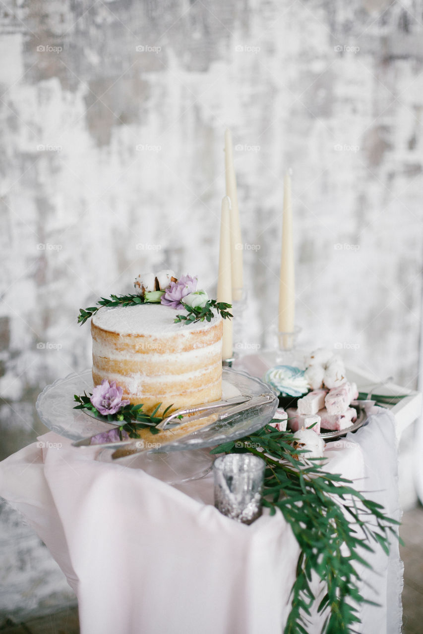 Beautiful wedding round cake with floral decorations and candles on glass cake stand.