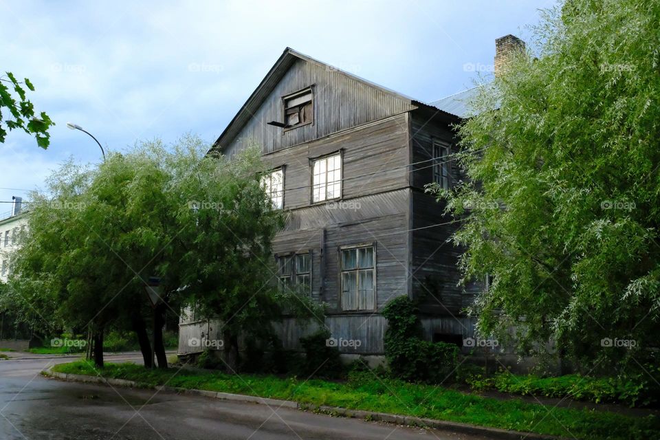 Rural wooden two-story house of gray boards surrounded by trees