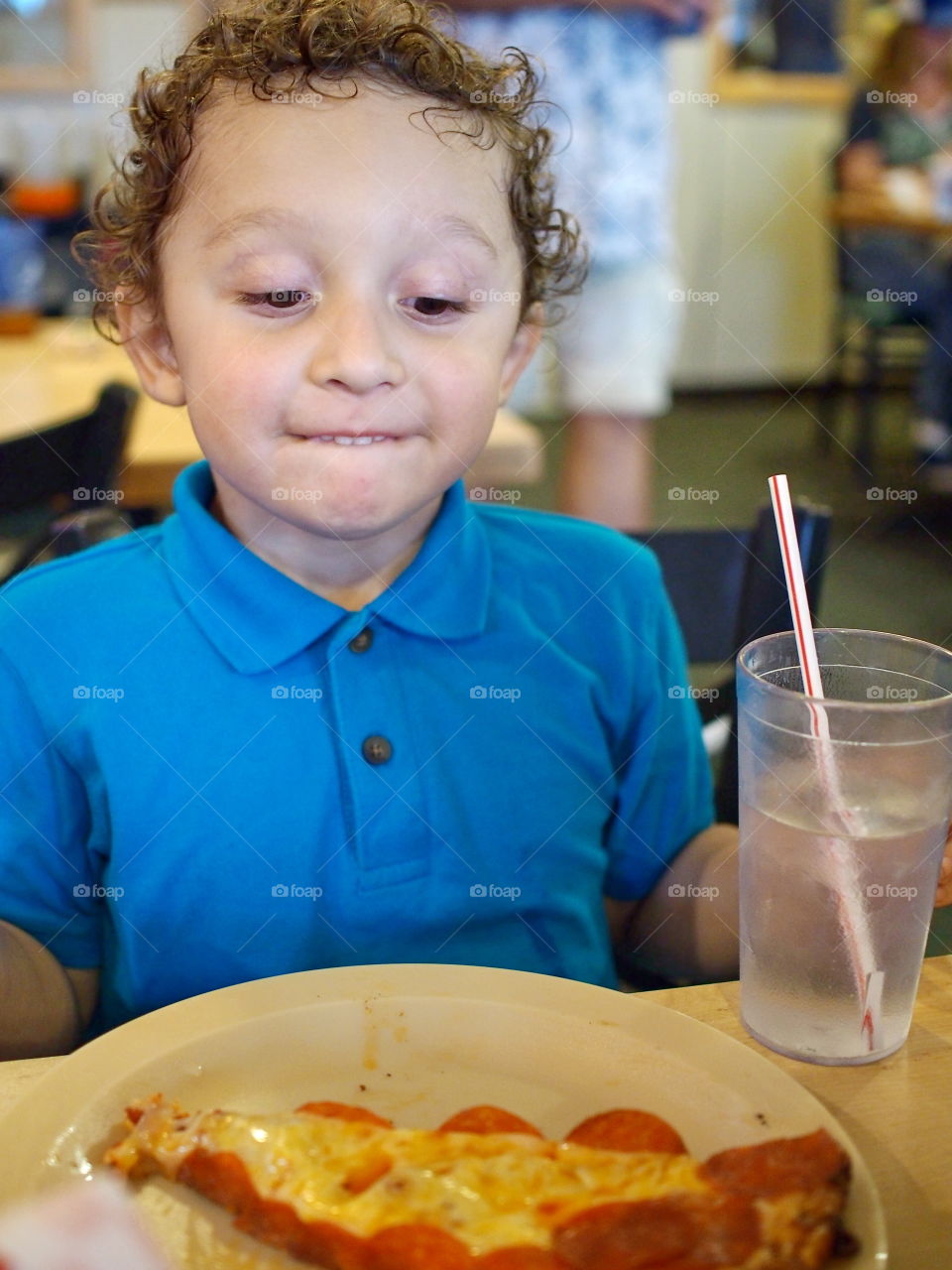 A little boy hungrily eyes his plate of pizza ready to dig in. 