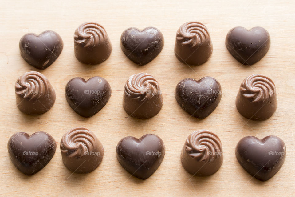 Dark chocolate hearts and milk chocolate swirls in  rows on wood.