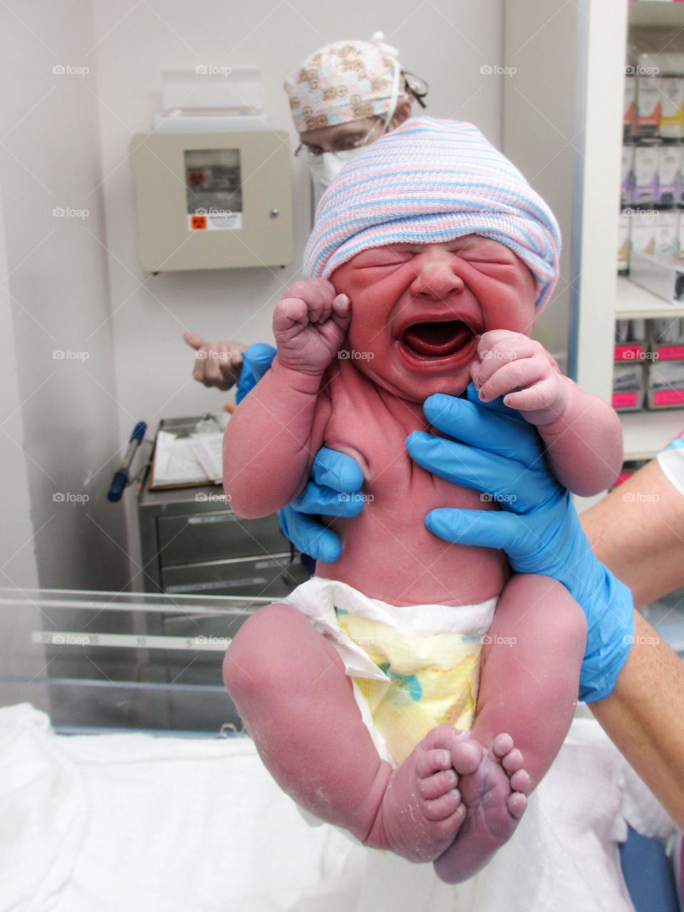 A doctor holding crying newborn baby in hands at hospital