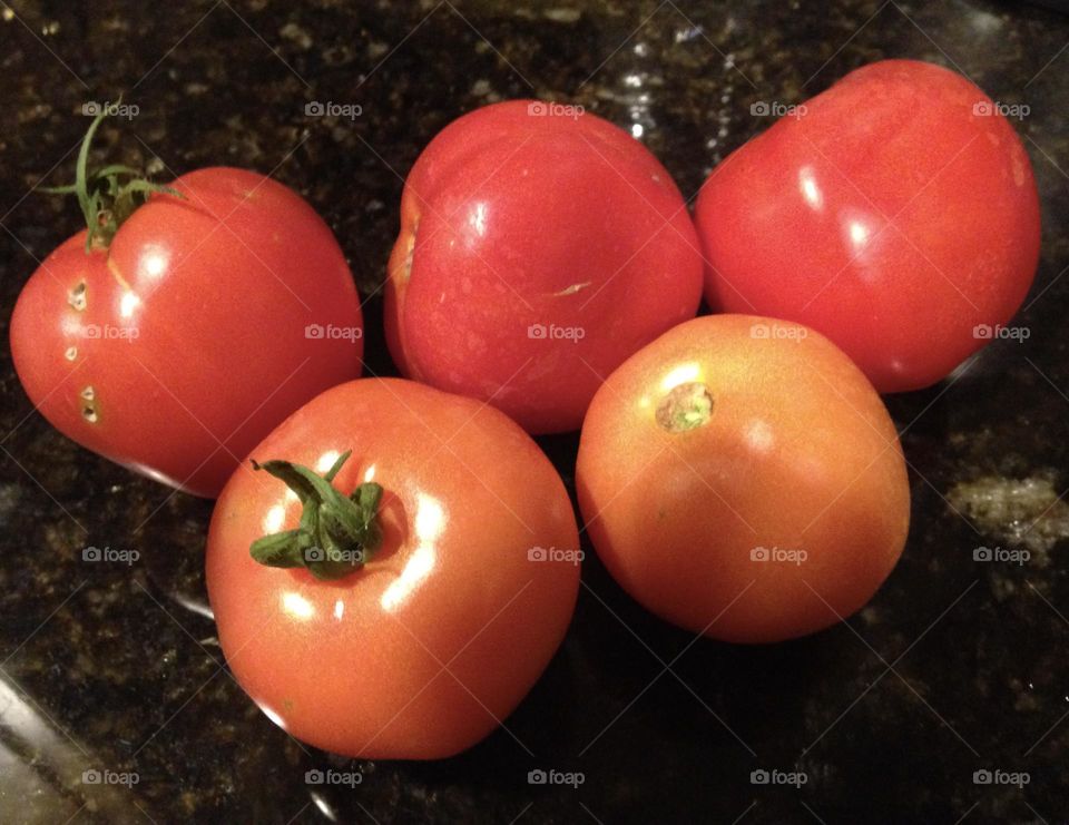 A group of garden-fresh tomatoes arranged on a sleek black quartz kitchen counter, their vibrant red color contrasting beautifully with the dark surface, showcasing their freshness and natural appeal.