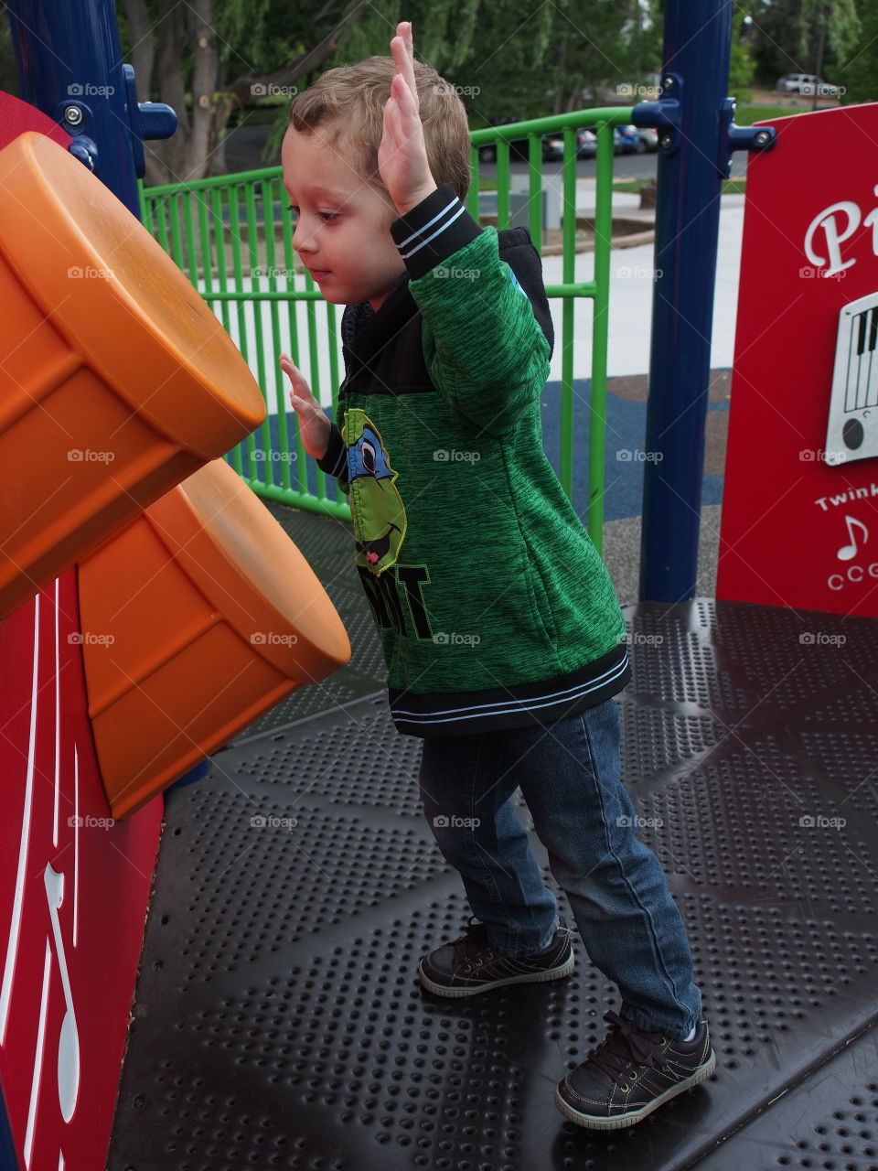 A little boy enthusiastically plays on the plastic drums on a play structure in the park. 