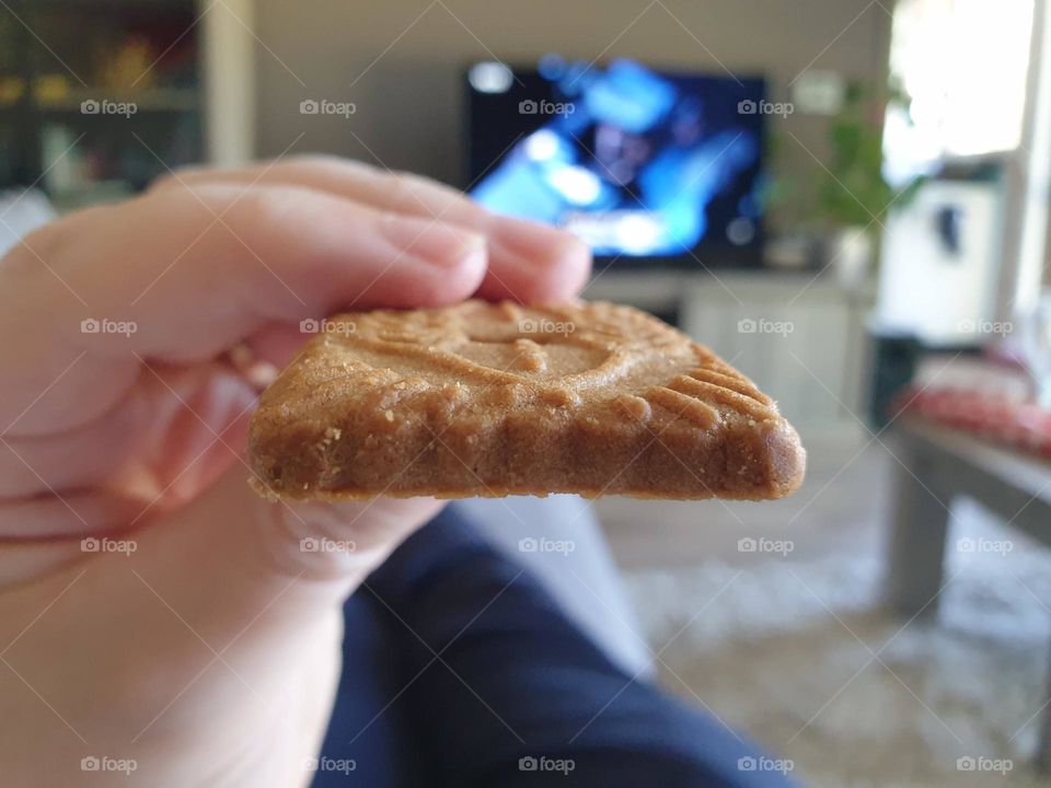 a portrait of someone holding a cookie in their hand ready to take a bite while watching tv.