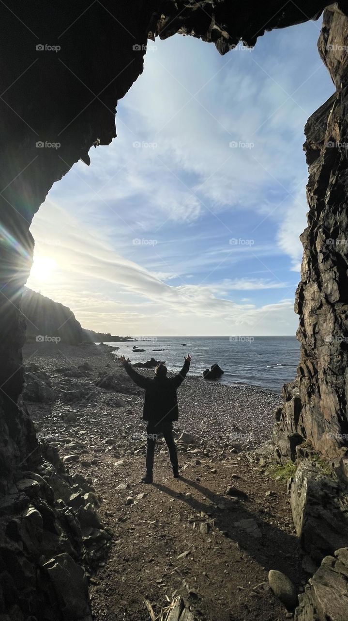 Welcome spring, man standing on the beach by the ocean reaching for the sky and the sunlight, shot taken from a cave 