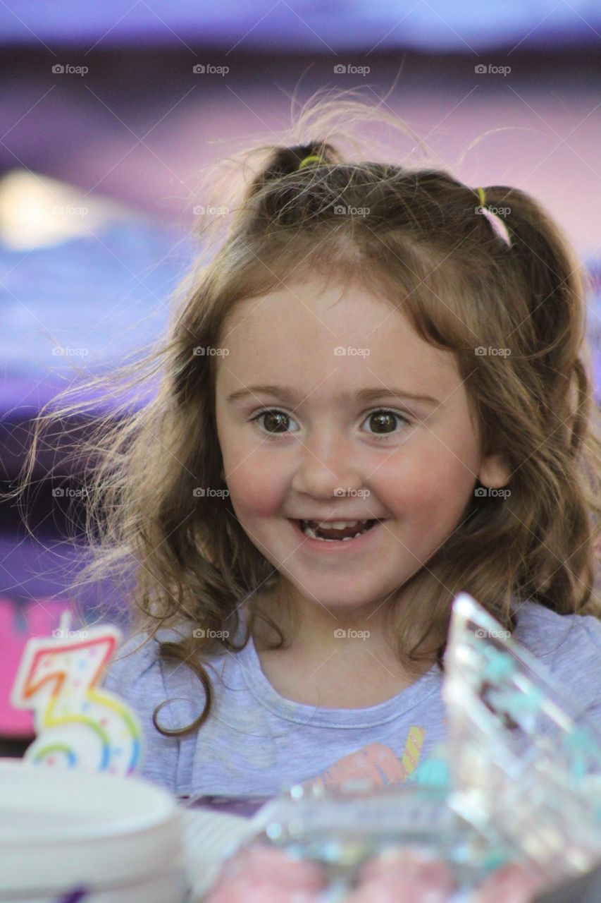 Toddler celebrating her 3rd birthday, smiling at her number 3 candle on her cake 