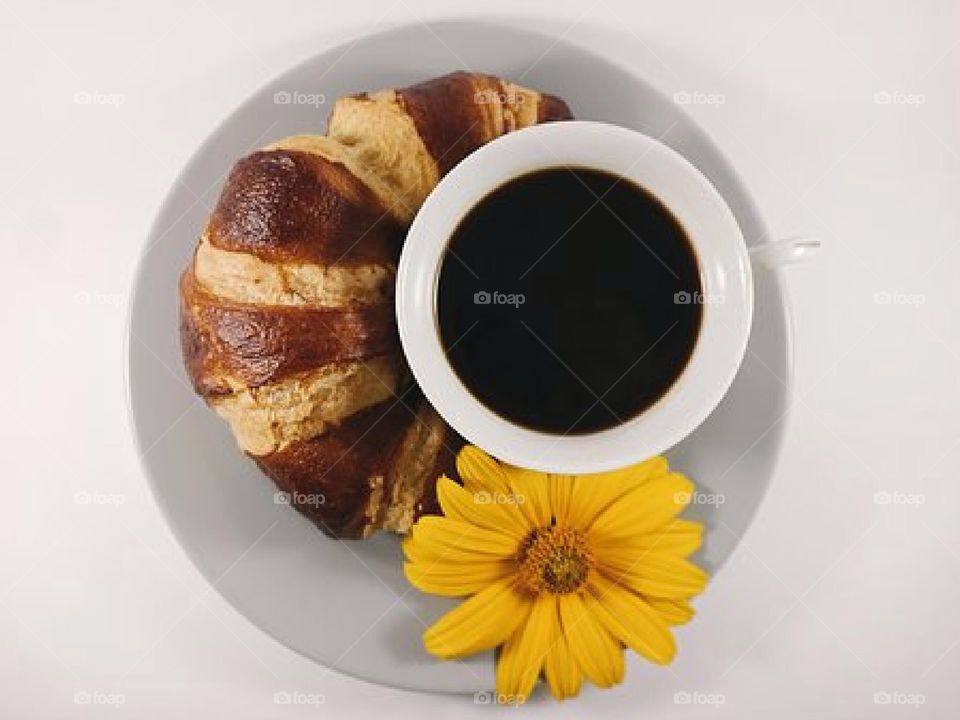 A cup of coffee with a bagel croissant.
