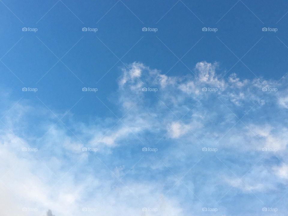 White clouds in blue skies, with what looks like a person (angel) waving 
